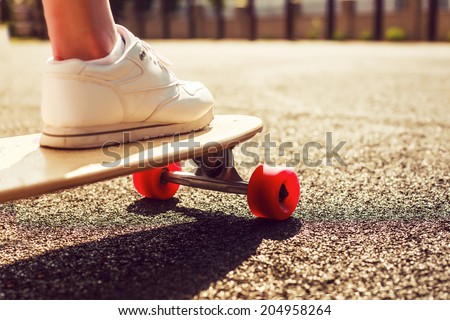 Longbard desk with red wheels on the road in summer sunny weather Girl ready to ride skateboard in the city