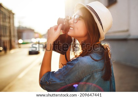 Outdoor summer smiling lifestyle portrait of pretty young woman having fun in the city in Europe in evening with camera travel photo of photographer Making pictures in hipster style glasses and hat