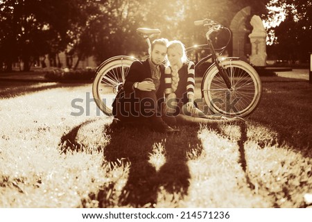 Pretty young vintage hipster couple in love sitting in the park in summer evening with old fashion bicycle and have fin on the grass