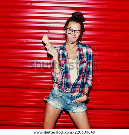 Outdoor night portrait of fashion sensual pretty crazy fashion brunette with ice-cream and sexy tongue in hipster style glasses on red background having fun alone
