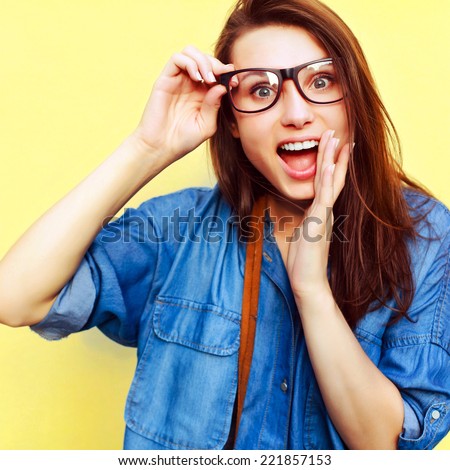 Pretty young smiling beautiful closeup portrait of sensual surprised woman in glasses with big eyes and open mouth on yellow background