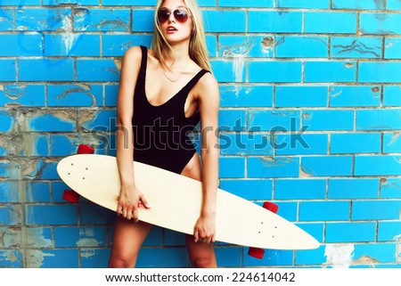 Outdoor summer portrait of young pretty sexy sport style blonde woman in blue pool with big longboard desk and have fun alone in hot weather