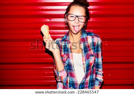 Outdoor closeup fashion portrait of young sexy crazy girl with long tongue and ice-cream on red wall background