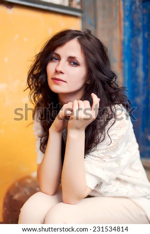 Outdoor spring colorful portrait of pretty young fashion brunette sensual woman sitting in the city on blue yellow background