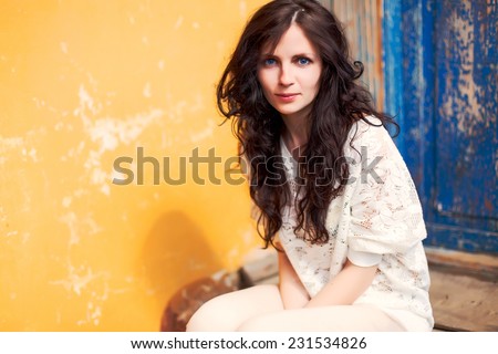 Outdoor spring colorful portrait of pretty young fashion brunette sensual woman sitting in the city on blue yellow background looks cute and happy