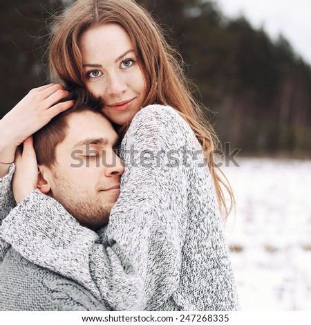 Sensual fashion beautiful outdoor winter portrait of young happy couple in love posing in snow field hugging each other and smiling