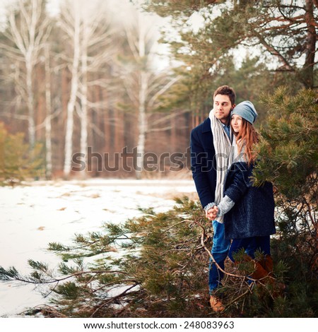 Outdoor beautiful photo of young fashion couple in love posing in cold winter forest feeling happy together