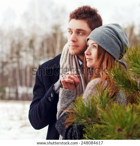 Outdoor winter portrait of happy couple in love posing in winter forest feeling happy together