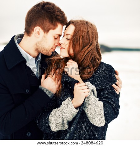 Outdoor fashion portrait of pretty young couple in love in winter cold weather feeling together happy