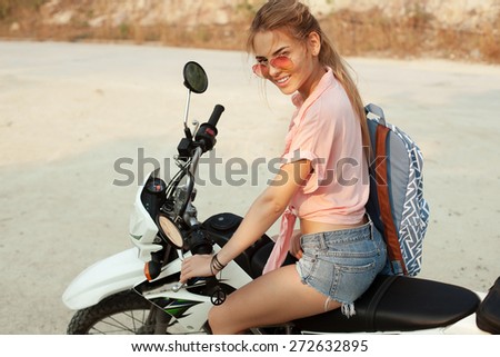 Outdoor summer portrait of young pretty blonde woman sitting on cross motorcycle traveling and having fun