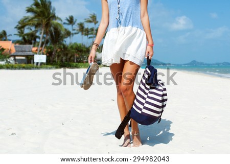 Young pretty sexy tanned woman standing on the beach and having fun outdoor on white sand with backpack and shoes
