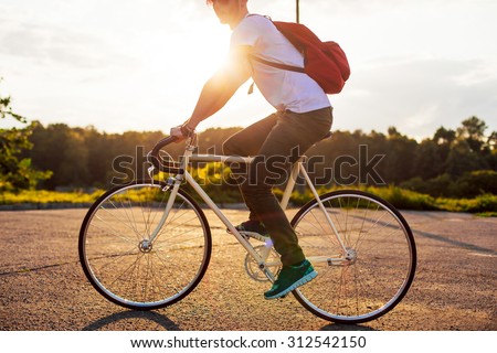 Outdoor urban style summer portrait of young handsome hipster man riding bicycle having fun on sunset