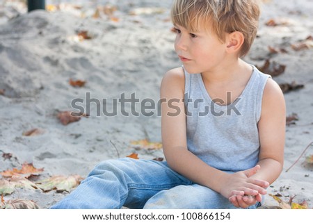 Little boy in deep thoughts playing in sandbox