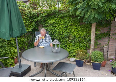 Retired senior Dutch man in deep thoughts whilst drinking a cup of hot coffee  in his back yard