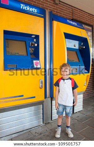 Smiling Little Dutch kid at train station in front of a ticket machine waiting for the train to go back to school and wearing a back pack