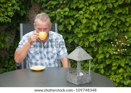 Retired senior Dutch man in deep thoughts drinking a cup of hot coffee in his back yard