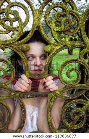 Scared woman trapped or locked behind an iron gate with moss and corrosion