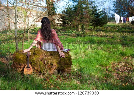 Girl sitting on a big wooden log and writing music for the banjo