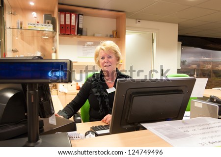Senior volunteer female cashier at work sitting at the museum front desk