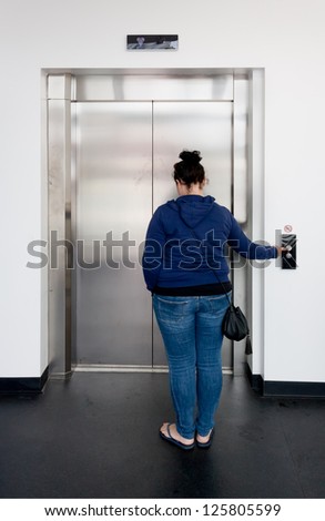 Young woman waiting in bright hallway and calling the elevator