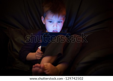 Little boy playing computer game late at night with blue lit face