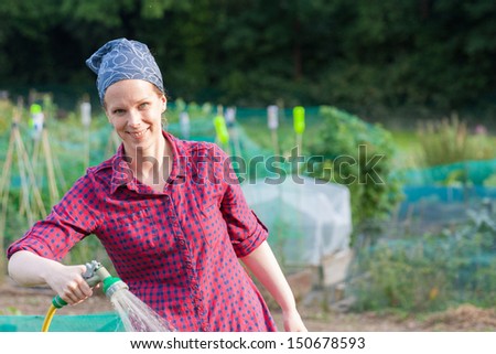 Smiling woman using a garden hose nozzle to water the allotment