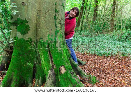 Man looking around a tree paying hide and seek in a forest