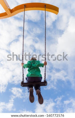 Young boy flying high on a swing against a blue sky with white clouds