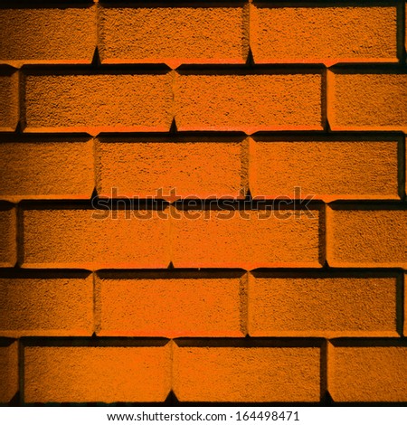 Brick wall made with big bricks lit up with orange lighting in square format frame