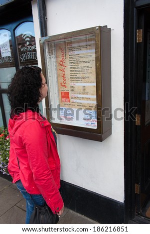 BUSHMILLS, NORTHERN IRELAND - AUGUST 17, 2012: Female tourist looking at the menu of one of many restaurants in Bushmills.  Bushmills cater for all types of tourists in city guest houses and B&B\'s.