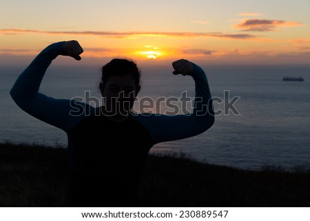 Silhouetted woman showing muscles at sunrise early morning