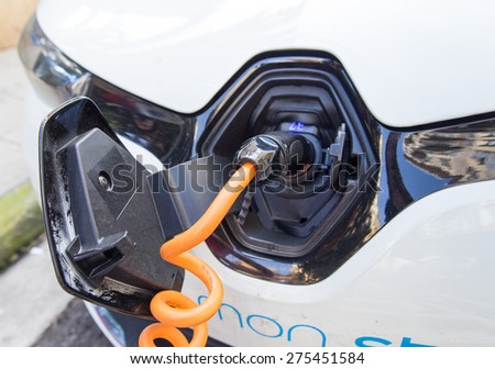 NICE, FRANCE - APRIL 11, 2015: An orange Auto Bleue charger cable is connected to a Renault Zoe electric car. The Zoe is a five-door supermini electric car produced by the French manufacturer Renault.