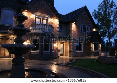 view of a large luxurious home in the evening after a light rain with a fountain in the front