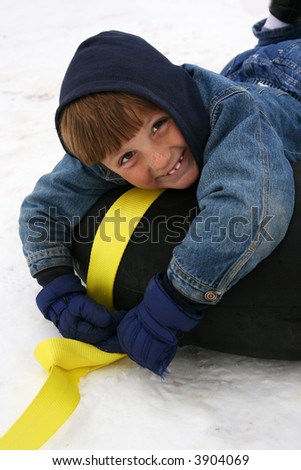 little boy dressed in winter gear on a black tube with a darling smile