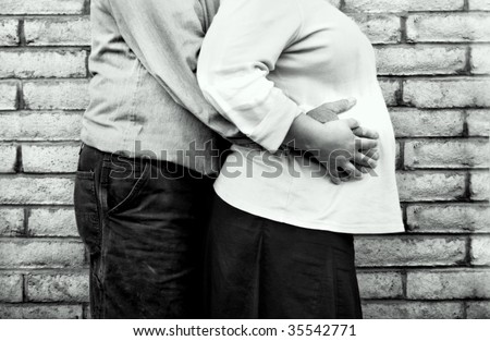 man putting arms around pregnant woman\'s belly against a brick wall background, black and white