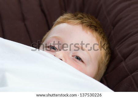 little boy peeping from under the duvet cover