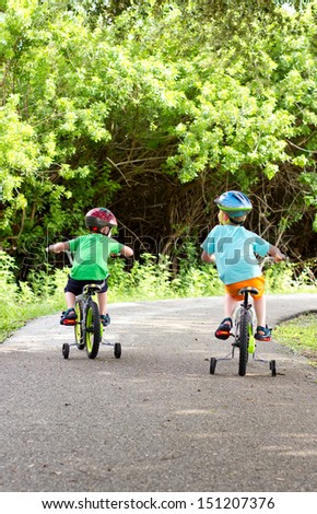 Two Little Boys Riding Their Bikes Along A Shaded Park Trail