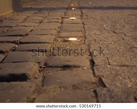 Picture of the cobblestone paved road with spotlight close up. Dark brown cobblestone road pattern close up. Selective focus on the middle of the picture.