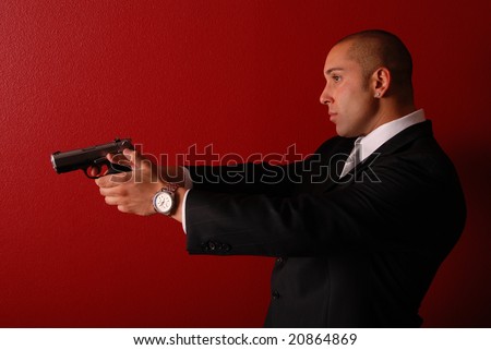 Profile view of a sexy man wearing a business suit holding a gun up in front of him.