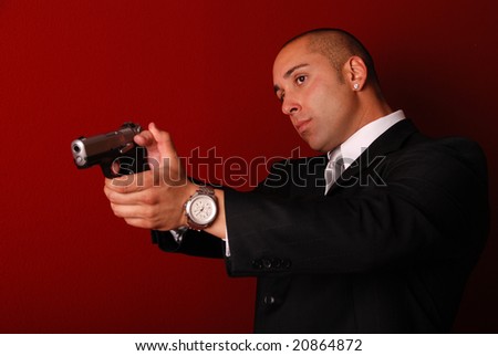 Attractive man wearing a suit aiming a gun. Red background.