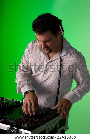 DJ wearing headphones by the mixing deck. Green gel over background light.