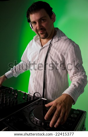 DJ wearing headphones with one hand on the mixing deck. Green gel over background light.
