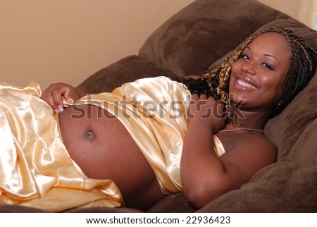 Beautiful pregnant African American woman, laying on a sofa wrapped in a gold satin sheet.