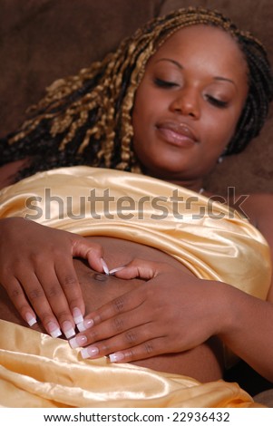 Pregnant woman making a heart shape with her hands over her belly.