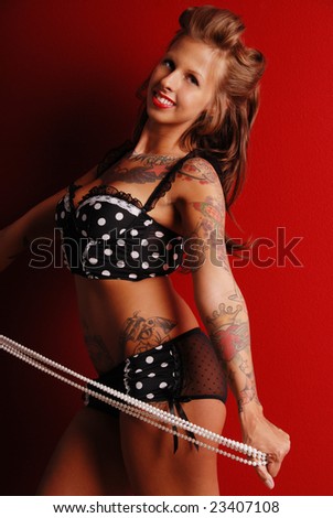 Sexy Pin-up girl wearing polka-dot lingerie posing by a red wall. She is holding a string of pearls.