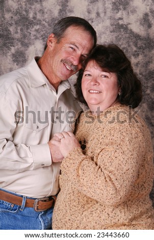 Portrait of a smiling middle aged couple. They are holding hands and pressing their heads close together.