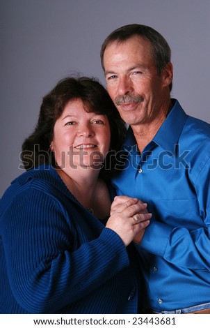 Portrait of a happy middle aged couple both wearing teal, holding hands.