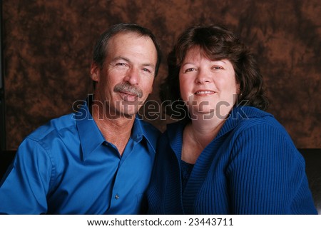 Portrait of a happy middle aged couple, wearing teal, against a brown mottled background.