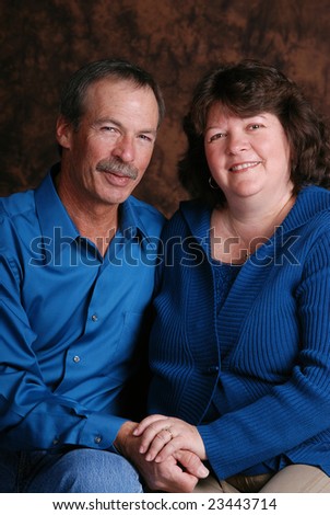 Portrait of a happy middle aged couple, wearing teal, against a brown mottled background.