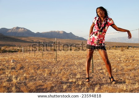 Sexy African American model posing against a wire fence in the desert in warm afternoon sunlight.